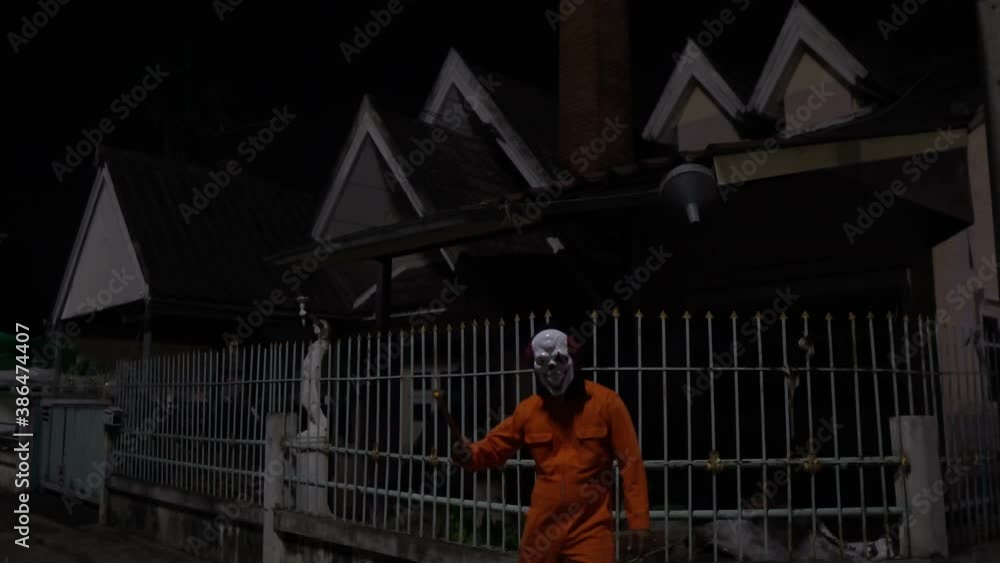 Asian handsome man wear clown mask with weapon at the night scene,Halloween festival concept,Horror scary photo of a killer in orange cloth Asian handsome man wear clown mask with weapon at the night scene,Halloween festival concept,Horror scary photo of a killer in orange cloth
