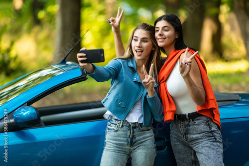 Two attractive young women taking selfe in a convertible car on summer day photo