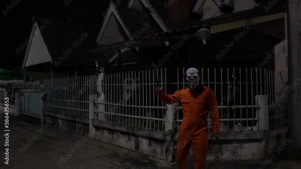 Asian handsome man wear clown mask with weapon at the night scene,Halloween festival concept,Horror scary photo of a killer in orange cloth Asian handsome man wear clown mask with weapon at the night scene,Halloween festival concept,Horror scary photo of a killer in orange cloth