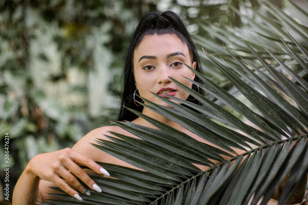 Natural beauty and people concept. Smiling pretty young Asian woman with black ponytail hair, posing to camera over tropical plants background, touching natural palm tree leaves Natural beauty and people concept. Smiling pretty young Asian woman with black ponytail hair, posing to camera over tropical plants background, touching natural palm tree leaves