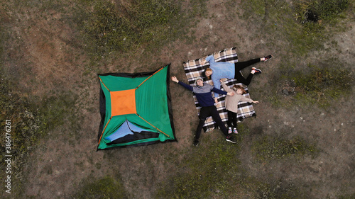 Aerial top view of family in campsite from above, parents and kid relax and lie on plaid, family camp vacation