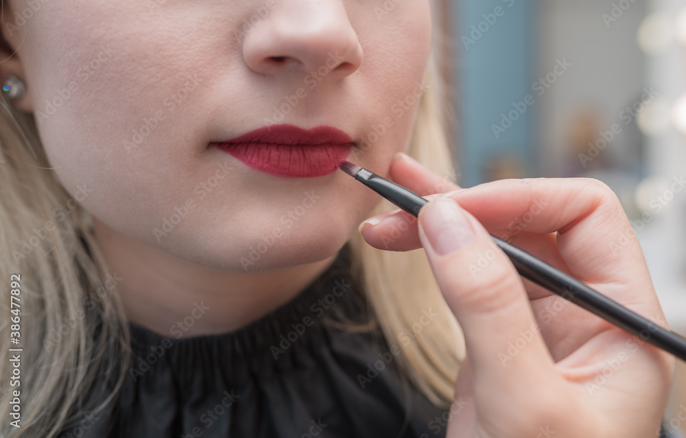 Professional makeup artist paints lips with red lipstick brush