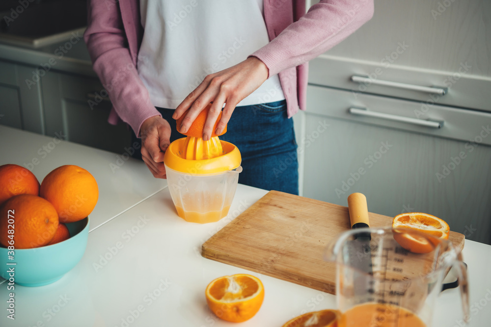 Close up photo of a caucasian woman squeezing fresh juice out of sliced oranges in the kitchen