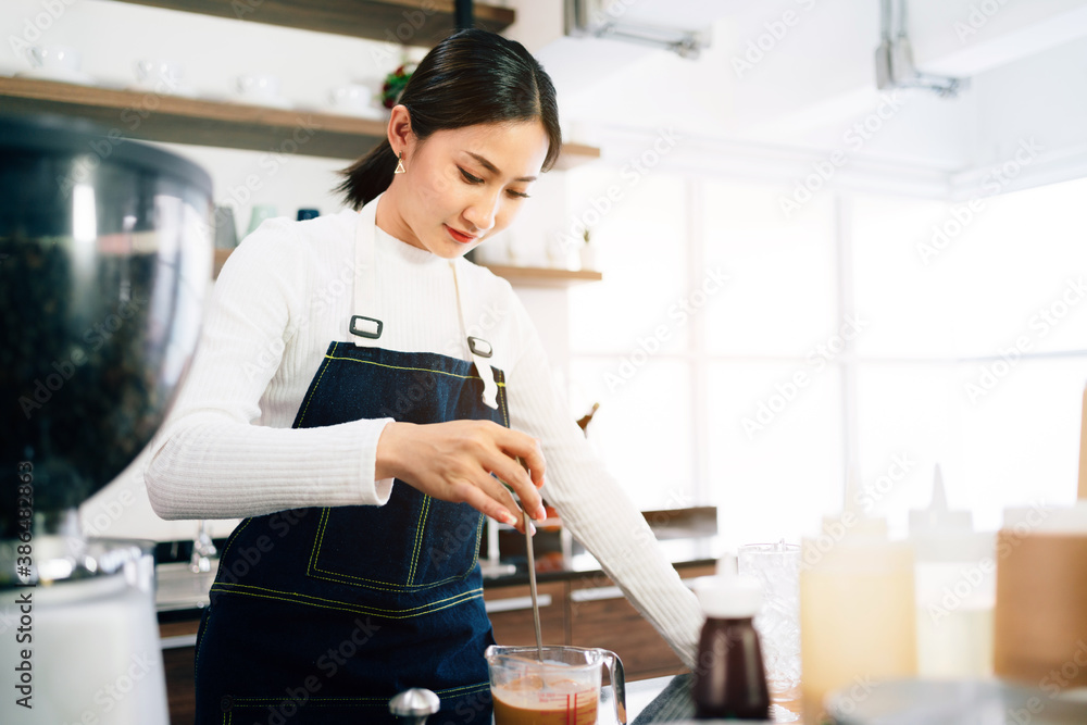 A female barista student attentively measured and added milk in the coffee while the teacher watching her in the coffee shop. Coffee making classes for entrepreneurs to start small businesses. A female barista student attentively measured and added milk in the coffee while the teacher watching her in the coffee shop. Coffee making classes for entrepreneurs to start small businesses.