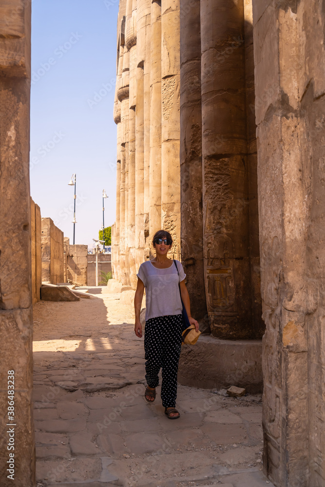 A young tourist in a white t-shirt and hat visiting the temple and looking at the ancient egyptian drawings on the columns of the Luxor Temple, Egypt