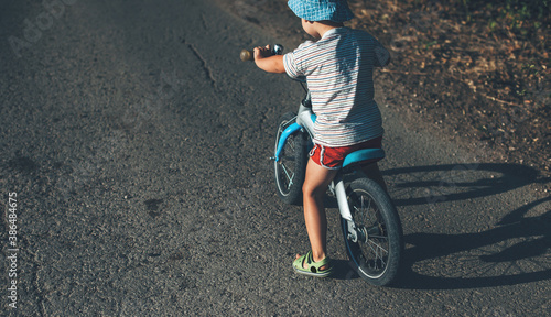 Caucasian boy with hat is learning to ride the bike on the road during a sunny summer day photo