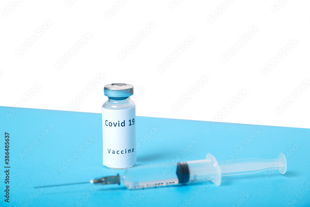A syringe and a vial with a virus vaccine are on a blue table, top view. A syringe and a vial with a virus vaccine are on a blue table, top view.