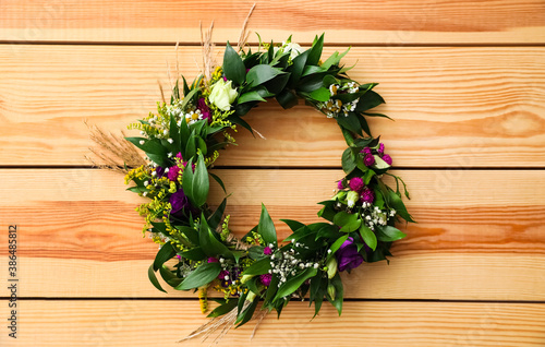 Beautiful wreath made of flowers and leaves on wooden background, top view