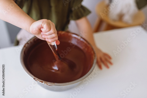 A little girl kneads chocolate dough for Christmas cookies with a large spoon.
