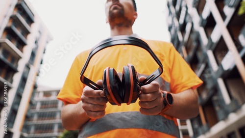 Construction worker with ear muff working at construction site. Worker puts on ear defenders to protect against sound. Taking care of health, safety at work. Earplugs. Too loud sound, hearing damage