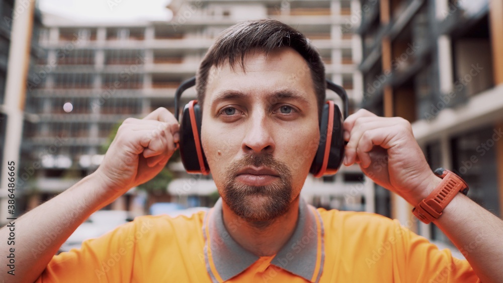 Man wearing safety equipment hearing protection. Worker wearing noise  cancelling ear defenders or ear muffs. Construction builder puts on protect  ears with headphones. Taking care safety during work foto de Stock