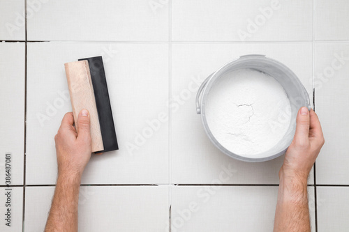 Worker hands holding rubber trowel and powder of grouting paste for ceramic tile seams on floor. Closeup. Point of view shot. Top down view. photo