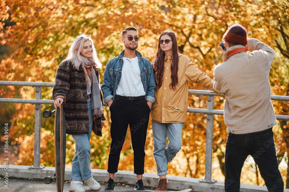Carefree and well dressed company of two guys and two girls having a good time and photographing in autumn background.