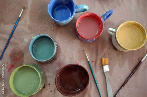 Multi colored image of an ceramic artist's painting table in wokshop from above with various colors inside hand made pots including green, red, yellow, brown, blue and turquoise with several brushes photo