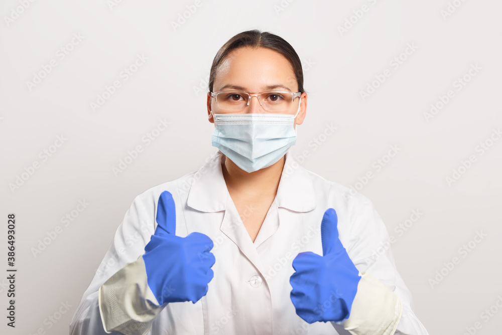 Woman doctor in protective mask and gloves shows thumb up gesture. Woman doctor in protective mask and gloves shows thumb up gesture.