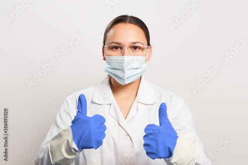 Woman doctor in protective mask and gloves shows thumb up gesture.