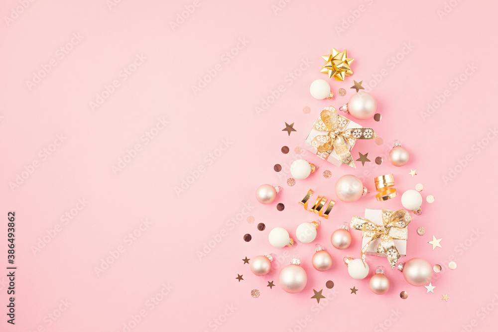 Christmas ornamets and gift boxes laid out in shape of Christmas tree on pink background