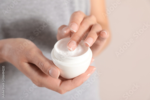 Young woman holding jar of cream on light background  closeup