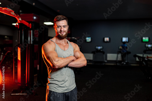 Full length of smiling sportive young man standing crosshands. Dark background of a modern gym. photo