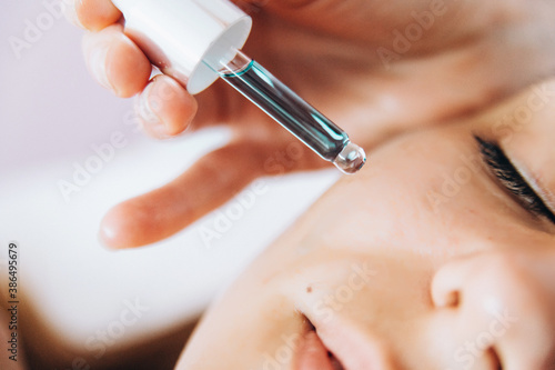Brunette young woman lying on the coach in beauty saloon.Woman in mask on face in spa salon. Having facial massage. Visiting beautician.Using serum closeup