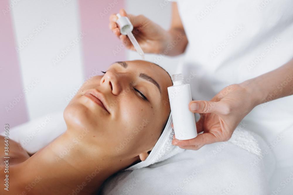 Brunette young woman lying on the coach in beauty saloon.Woman in mask on face in spa salon. Having facial massage. Visiting beautician.Using serum. Brunette young woman lying on the coach in beauty saloon.Woman in mask on face in spa salon. Having facial massage. Visiting beautician.Using serum.