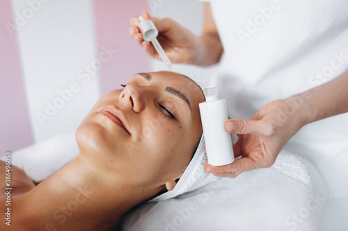 Brunette young woman lying on the coach in beauty saloon.Woman in mask on face in spa salon. Having facial massage. Visiting beautician.Using serum.