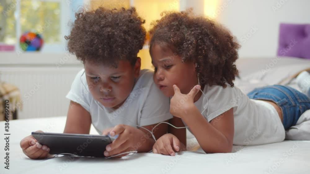 Portrait of adorable african boy and girl kids watching cartoon in earphones on digital tablet Portrait of adorable african boy and girl kids watching cartoon in earphones on digital tablet