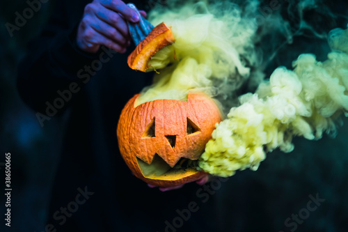 Chico joven con mascarilla por covid 19 con calabaza de halloween con humo amarillo