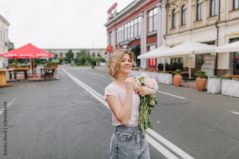 Happy girl with a bouquet of peonies walking through a deserted city in the early morning