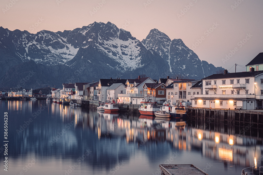 Naklejka premium charming view of small village at night after sunset in Lofoten. Water surface of harbor was quiet and peaceful, so the reflection of mountains and houses was clear and amazing