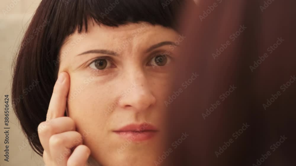 Young Woman Examines First Wrinkles on her Face, Looking at Herself in Mirror. Young Woman Examines First Wrinkles on her Face, Looking at Herself in Mirror.