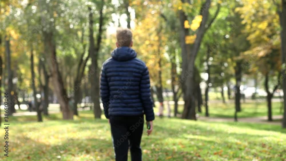 A young guy with a smartphone in his hand slowly walks into the distance of the autumn park, view from the back. Autumn concepts of loneliness, sadness or bad mood, copy space for text. A young guy with a smartphone in his hand slowly walks into the distance of the autumn park, view from the back. Autumn concepts of loneliness, sadness or bad mood, copy space for text.