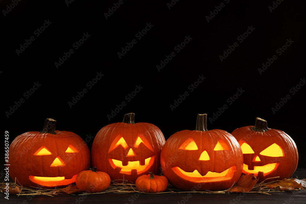 Glowing jack o'lanterns on table in darkness, space for text. Halloween decor Glowing jack o'lanterns on table in darkness, space for text. Halloween decor