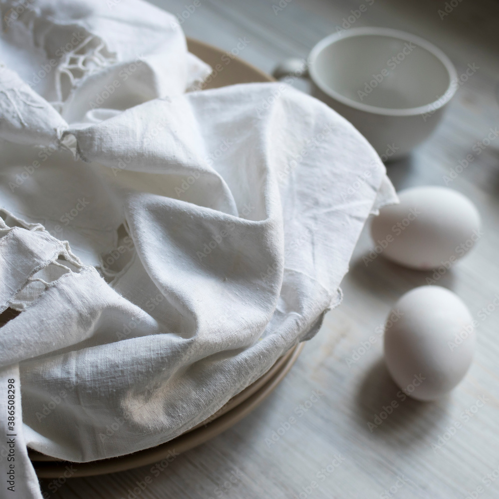 a stack of plates with an embroidered crumpled napkin, two eggs and two empty tea cups on a gray wooden kitchen table a stack of plates with an embroidered crumpled napkin, two eggs and two empty tea cups on a gray wooden kitchen table