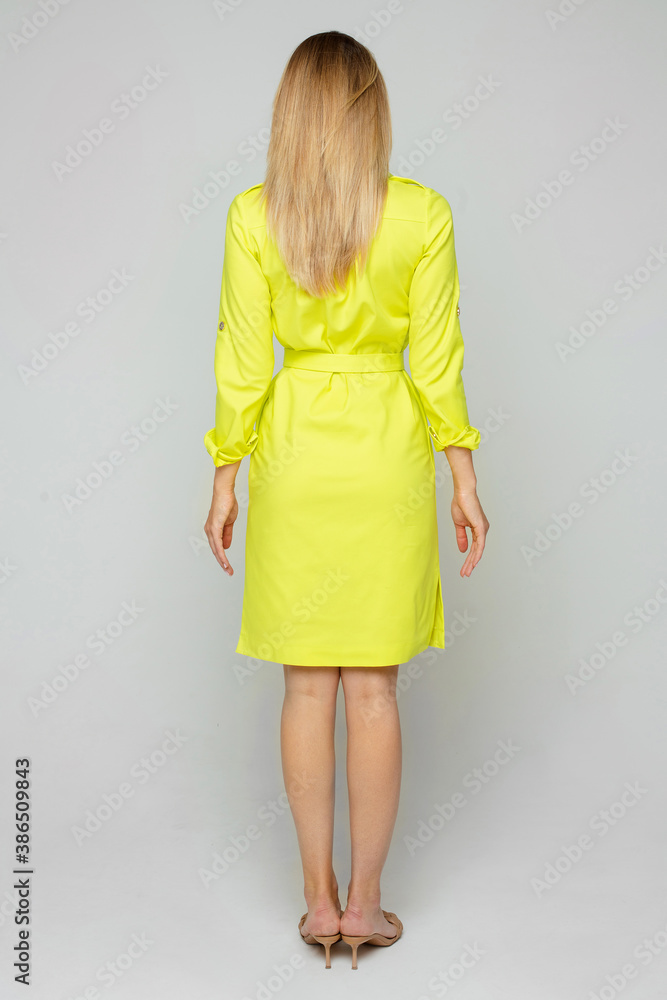 Picture of the back of caucasian female with wavy blonde hair, soft skin in yellow dress keeps her hands on the waist Picture of the back of caucasian female with wavy blonde hair, soft skin in yellow dress keeps her hands on the waist