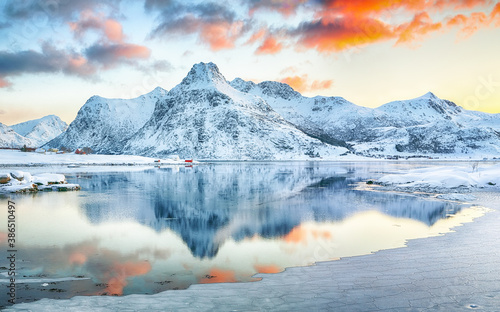 Frozen Flakstadpollen and Boosen fjords with red rorbuers and reflection in water during sunrise with Hustinden mountain on background.