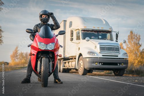 Motorbiker is standing on the countryside road on a truck background.