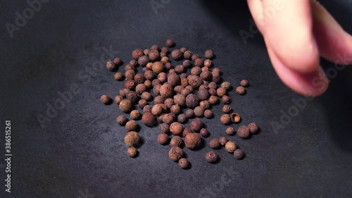 Close up of human hand putting dried pimento grains into dark grey cast iron pan for roasting spices photo