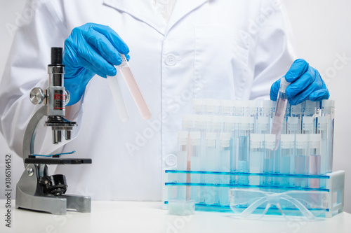 Canvas Print Close-up view of scientist in blue protection gloves puts biological tubes with covid-19 vaccine with microscope on laboratory room background