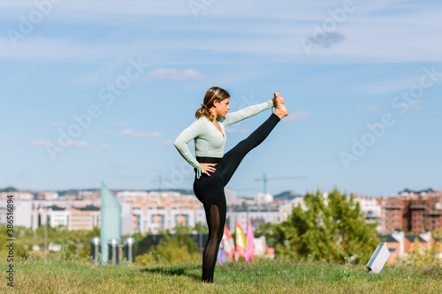 Young sport woman stretching to practice yoga in garden with landscape background
