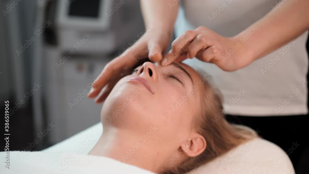 Woman masseur makes face relaxing massage to young beautiful female client blonde and spa treatment for perfect skin in beauty salon. Cosmetology services. Skin and body care and Healthcare Woman masseur makes face relaxing massage to young beautiful female client blonde and spa treatment for perfect skin in beauty salon. Cosmetology services. Skin and body care and Healthcare