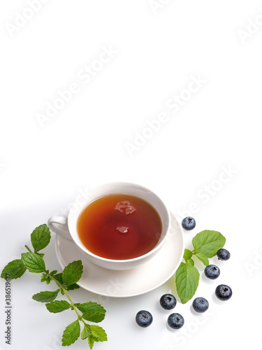 A Cup of black tea on a saucer with mint leaves and blueberries on a white isolated background. Copy space