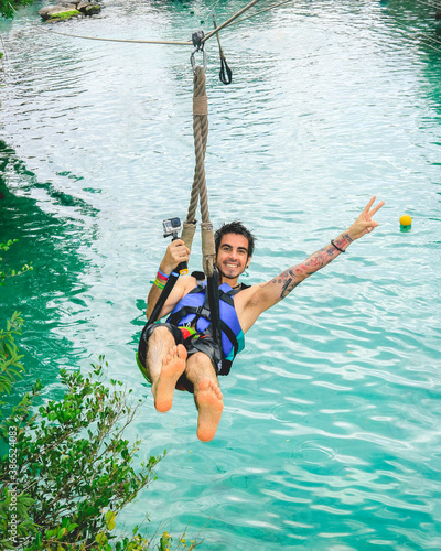 Happy guy with swimwear in a zipline over the caribbean sea photo