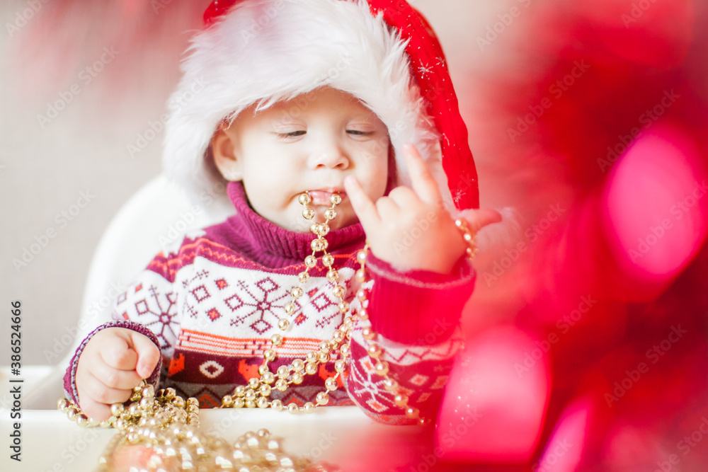 A little baby girl in a New Year's hat of Santa Claus examines and plays with New Year's decorations.