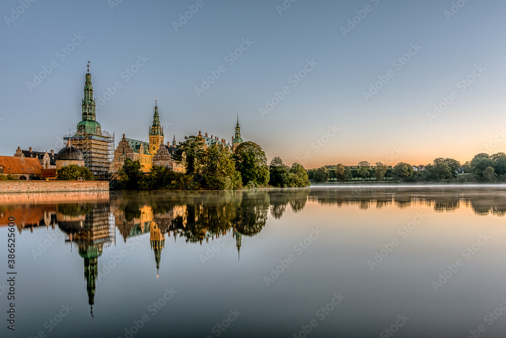 the calm lake of Frederiksborg with reflections of the castle at sunrise