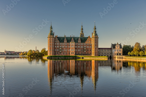 Frederiksborg castle glimmers in the sunshine and is reflected in the mirror-shiny lake