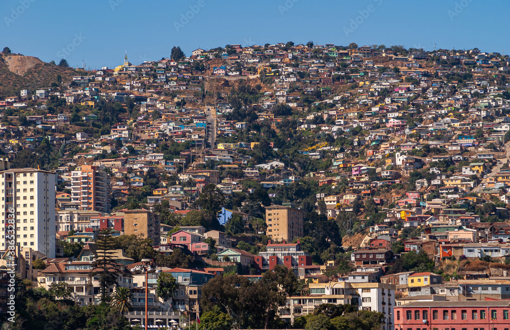 Valparaiso, Chile - December 8, 2008: Hill flank above bay is covered by dense housing, dwellings and apartment buildings in multi colors, styles, and quality under blue sky.