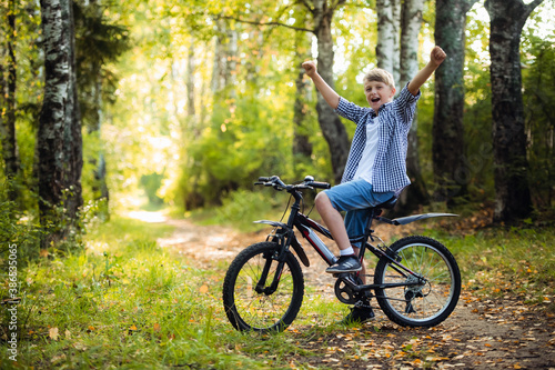 Joyful boy on a bicycle with a hands raised in the park © romankosolapov