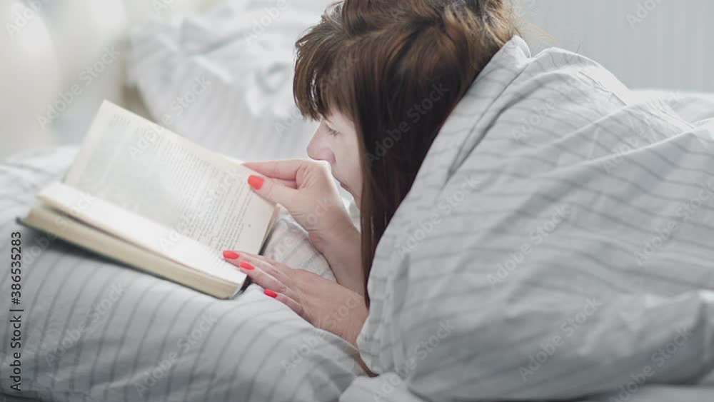 woman lies on the bed near the window and reads a book in the morning woman lies on the bed near the window and reads a book in the morning
