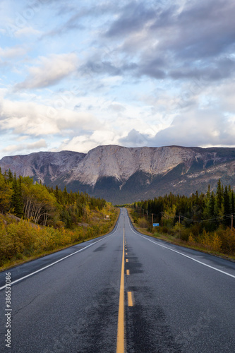 View of Scenic Road surrounded by Trees and Rocky Mountains on a Cloudy Fall Day in Canadian Nature. Taken near Whitehorse, Yukon, Canada.